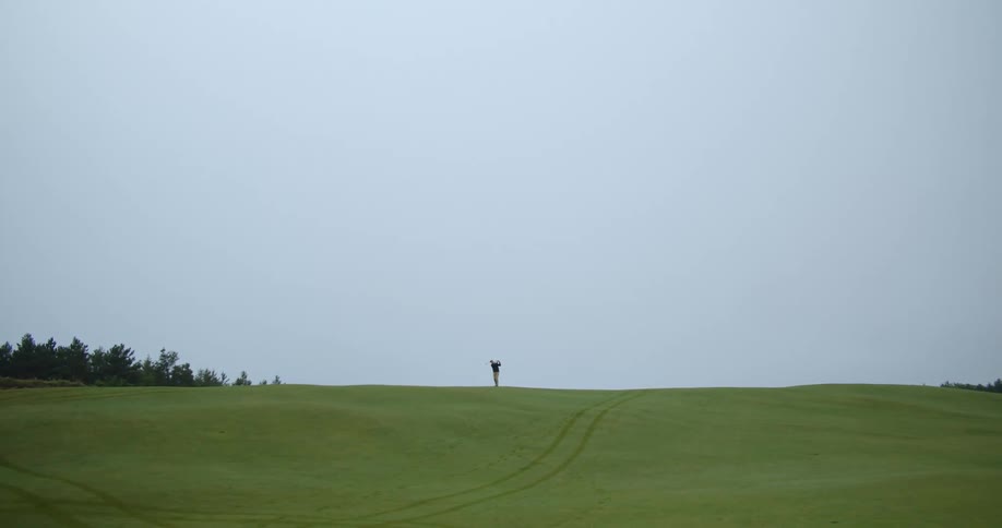 A person takes a golf swing in the distance