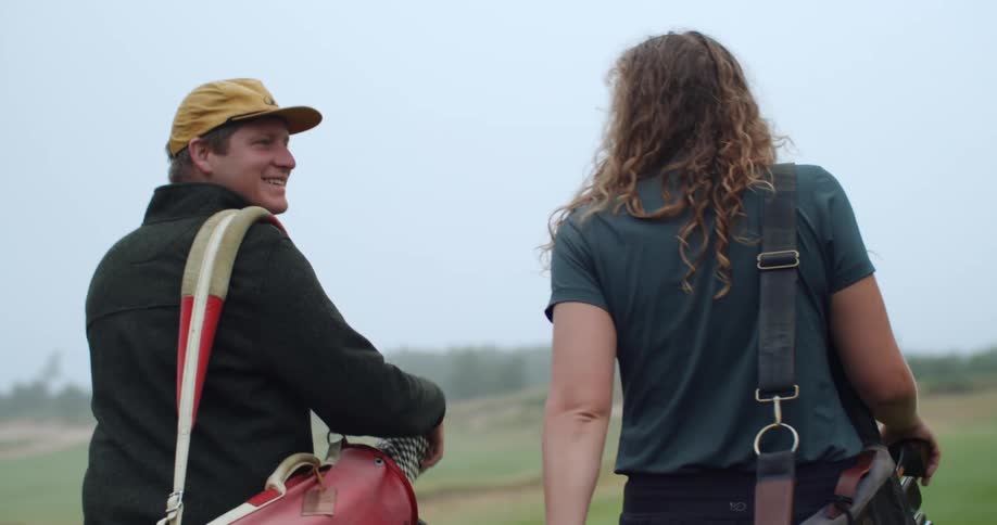 A man and woman fist bump while walking on a golf course