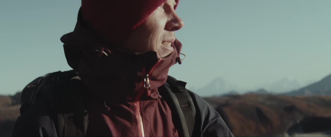 Man hikes with pair of walking sticks looking over scene with peak in the background