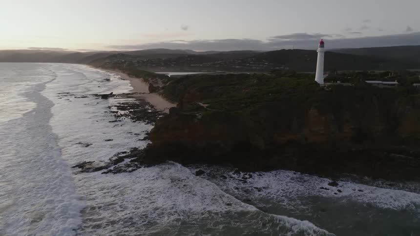 A lighthouse flashes as waves crash below