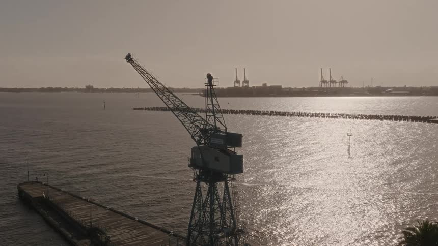 Loading cranes sit on dock near coast as waves reflect sunlight