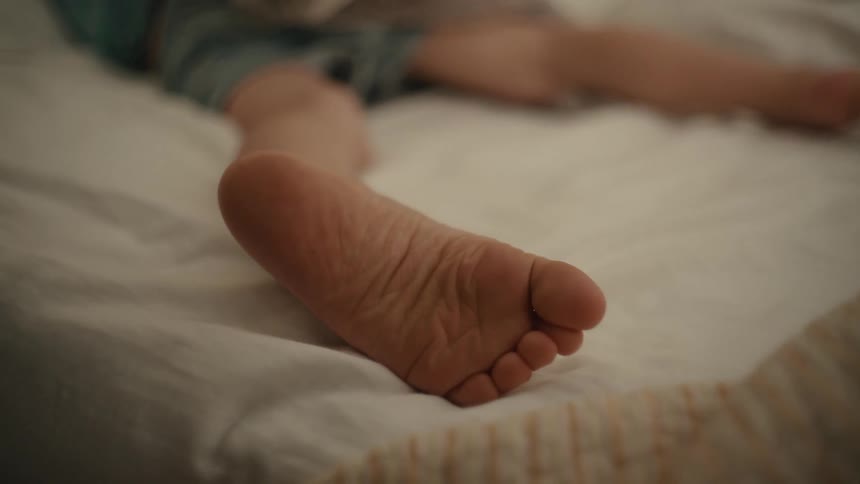 Young person lies on bed moving their barefoot around