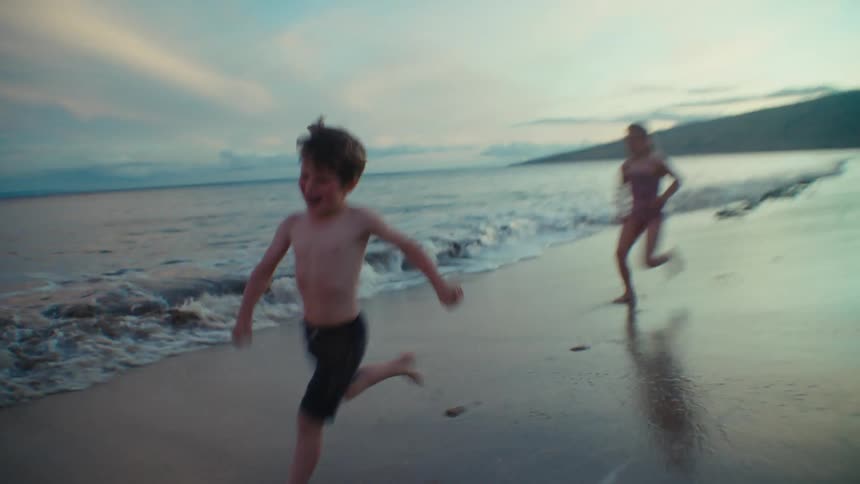 Brother sister and mom run along the beach at dusk near the ocean