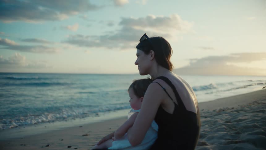 A woman holds her toddler while sitting on the beach