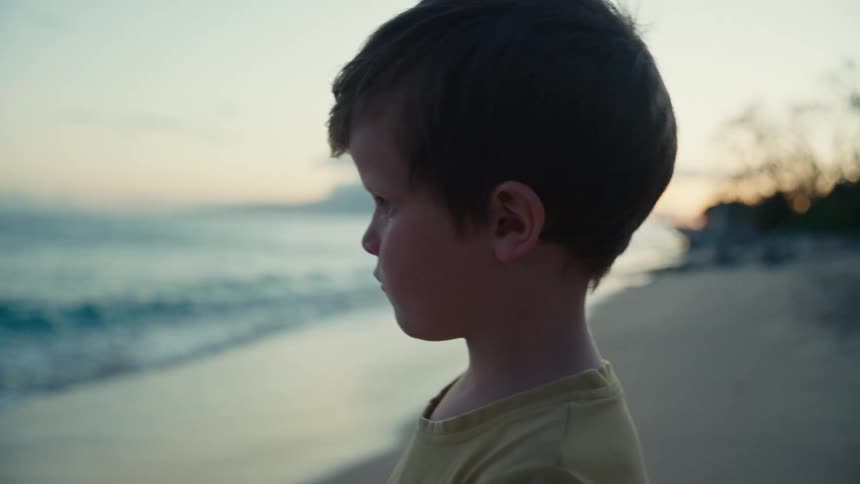 A young boy stares at the ocean on a beach