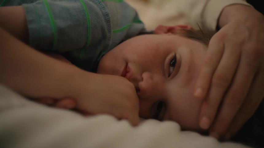 Mother checks temperature of son lying down and coughing