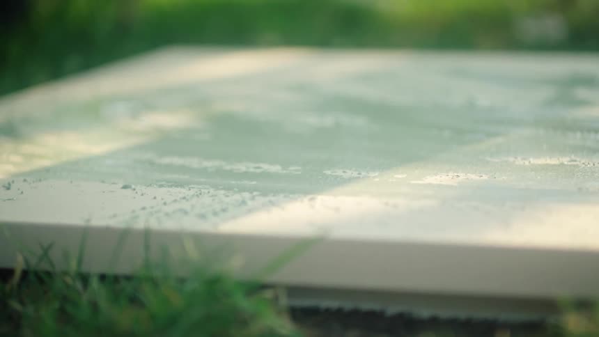 Paintbrush applies paint to surface of canvas lying on lawn
