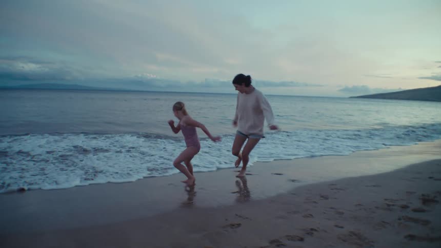 Mother and daughter play on the beach at dusk near the sea