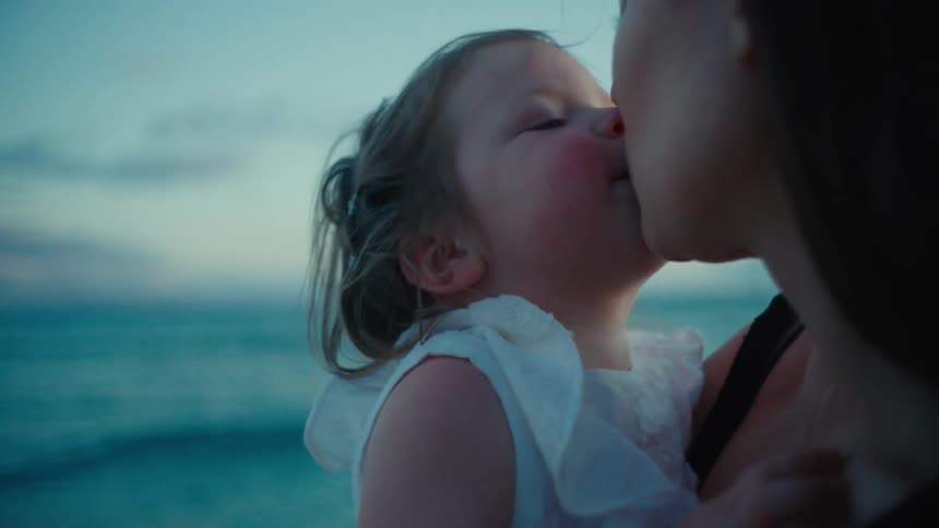 A woman kisses her daughter while standing along the coast
