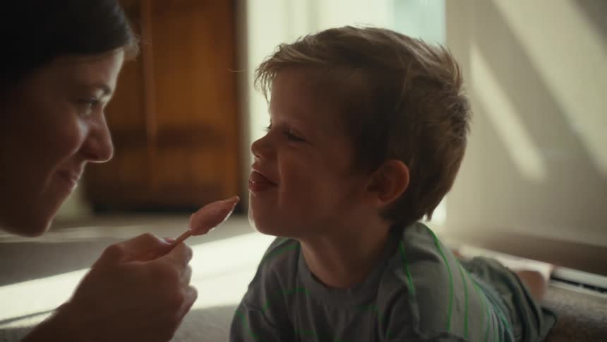 A woman and a toddler are on the floor in front of each other sharing an ice cream
