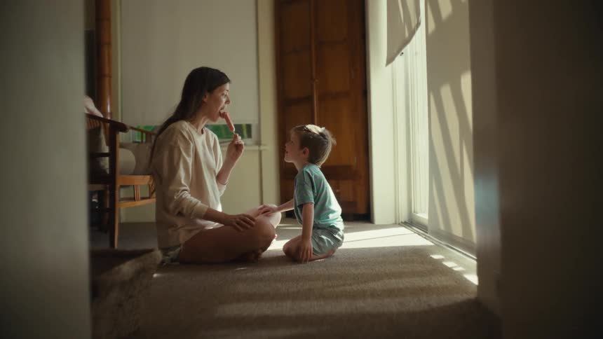 Mother and son sitting on the floor share ice cream in room