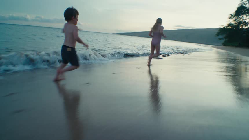 Boy and girl run across beach near surf