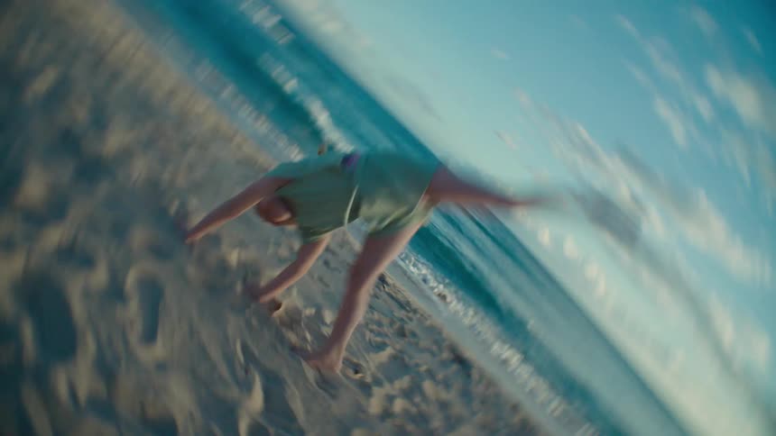 A young girl performs a cartwheel on the beach as the camera spins in sync with her movement