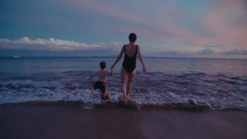 Mom and young son run into the ocean while holding hands