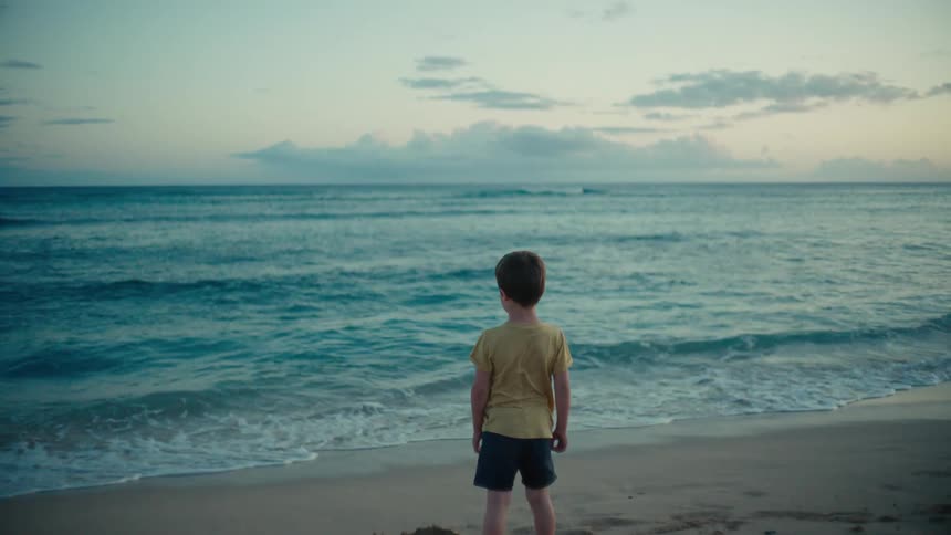 A boy on a beach stares at the sea