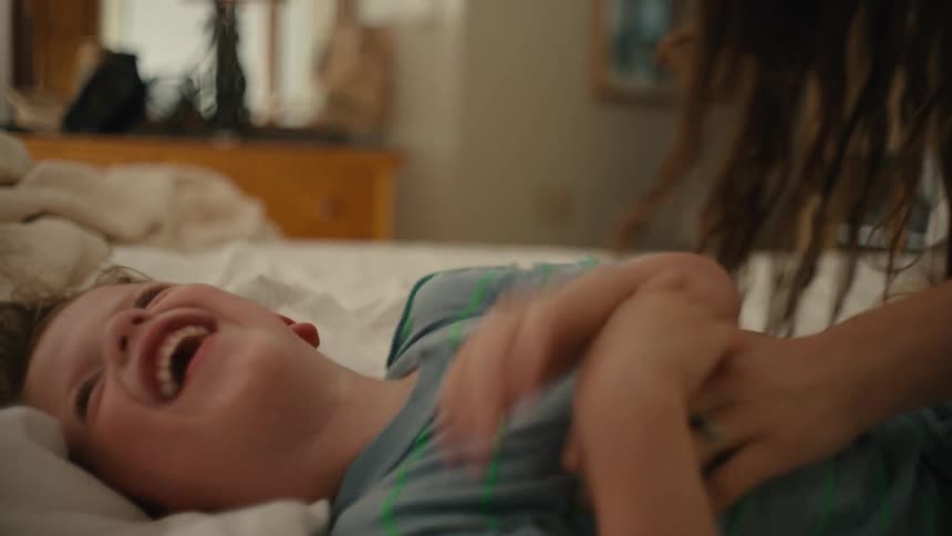 Mother tickles son lying on bed laughing