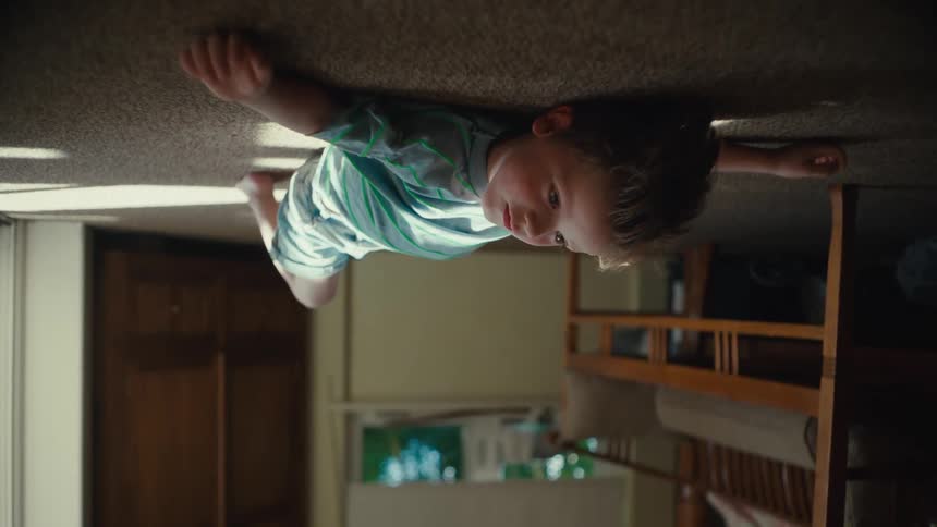 An upside down view of a toddler lying on a carpeted floor as he looks up to the ceiling points and speaks