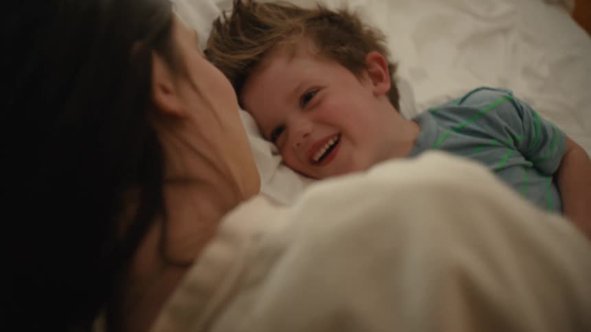 A mother and son laugh in bed