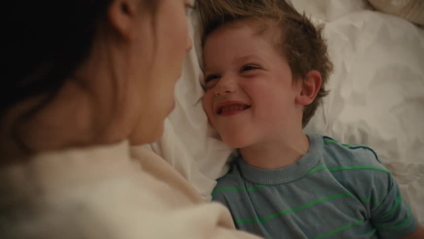 Mother and son play with each other on bed laughing
