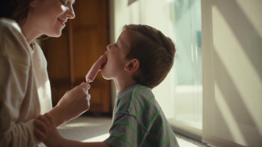 Mother and toddler son share an ice pop while laughing and being happy