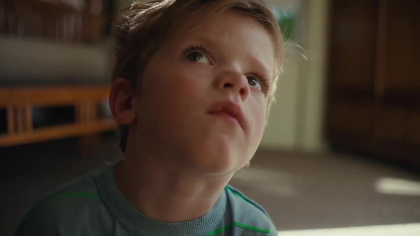 A toddler sitting on the floor of his room stares at the ceiling intently