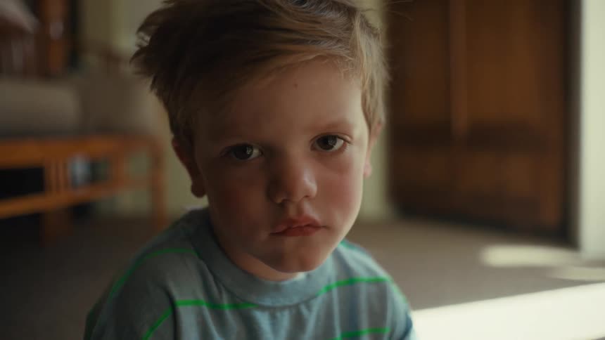Blonde toddler boy frowns and then smiles at camera