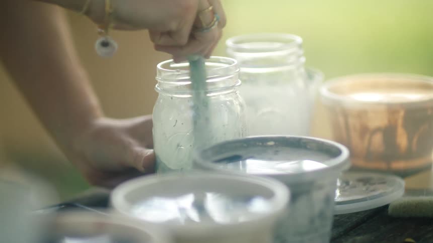 Close up of painters hands stirring paint in a jar