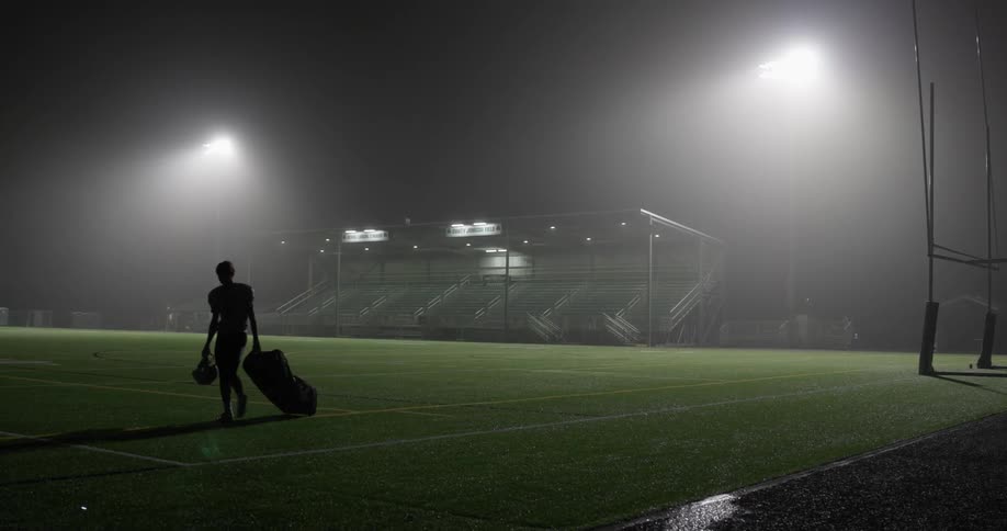 Athlete drags bag off brightly lit football field at night