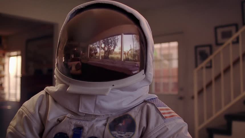 Astronaut stands in home wearing a spacesuit with a helmet reflecting window