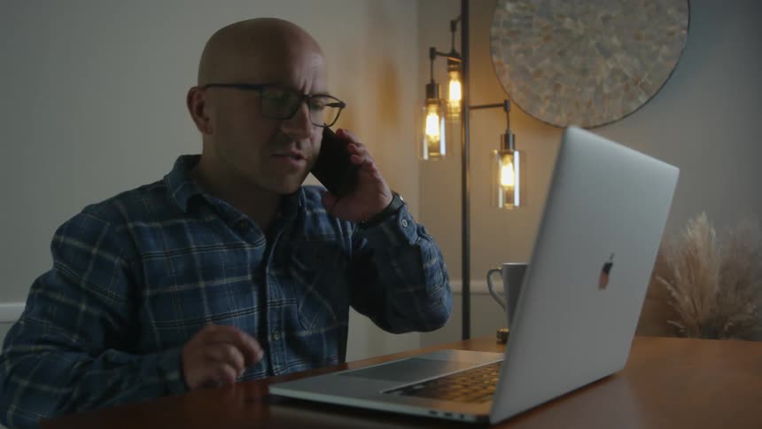 Man consults laptop while talking on smartphone