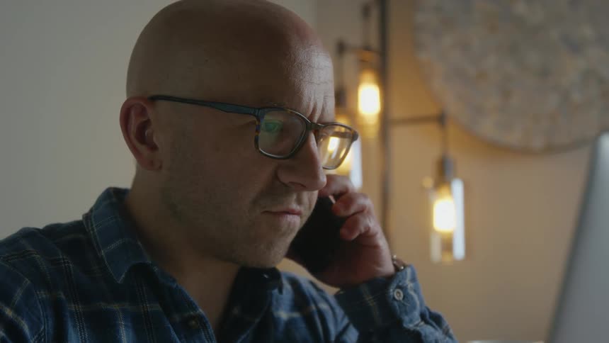 Man consults laptop while talking on smartphone