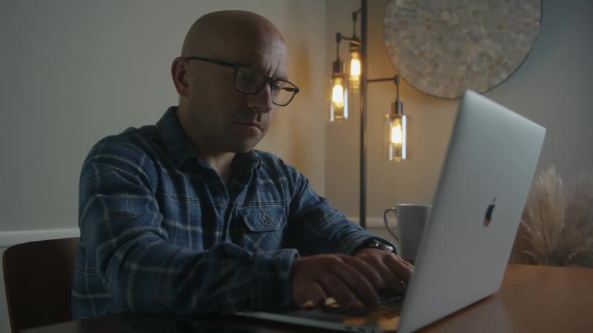 Man sits at table typing on apple laptop