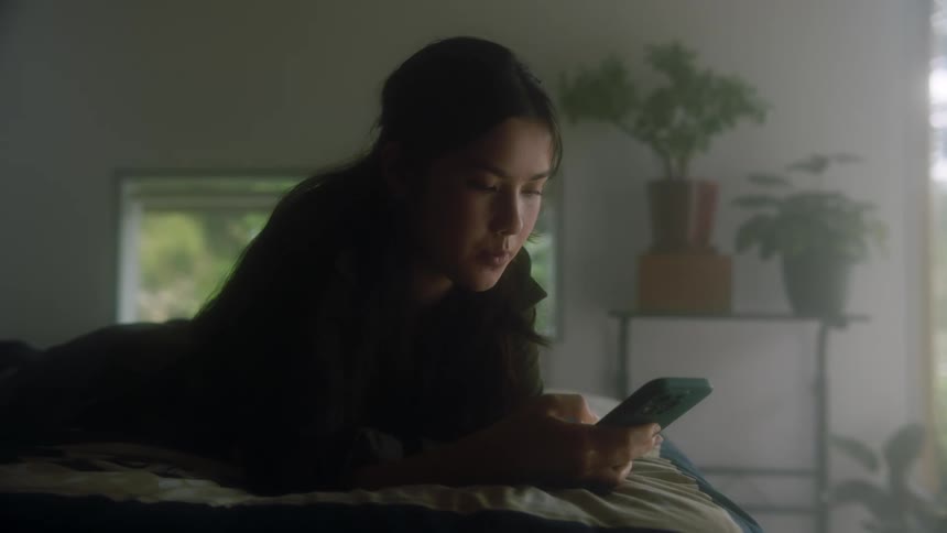 Woman lies on the bed and scrolls on smartphone