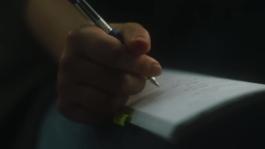 Woman sits and makes notes in notebook on her lap