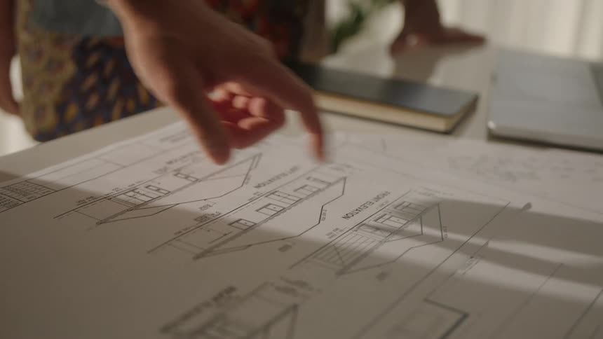 People stand around table near window discussing house plans