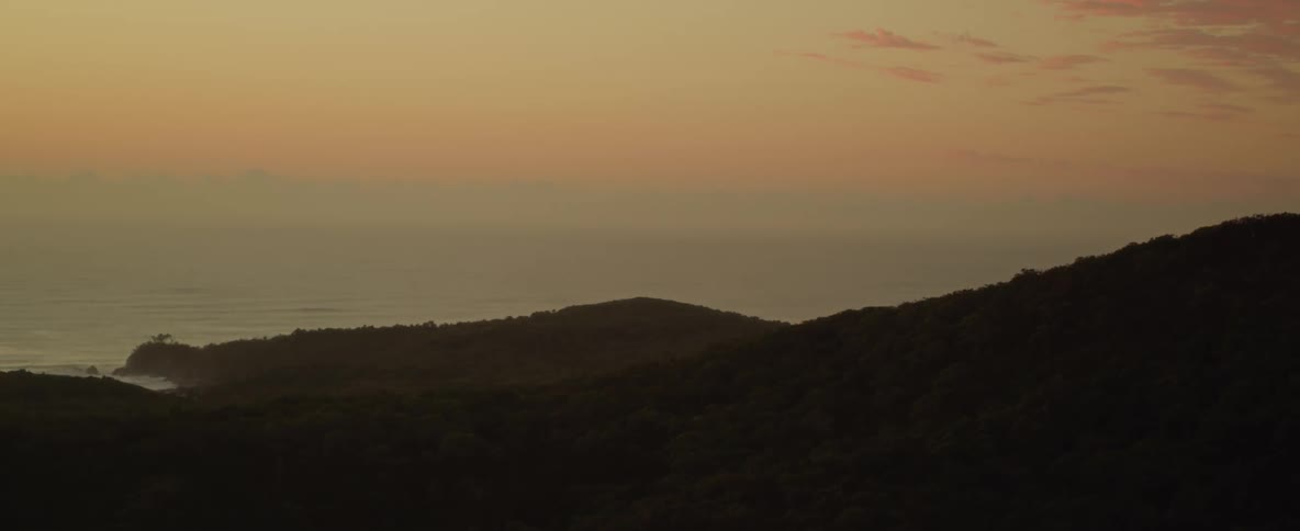 An aerial silhouette of hills leading to the coast with the ocean on the horizon landscape