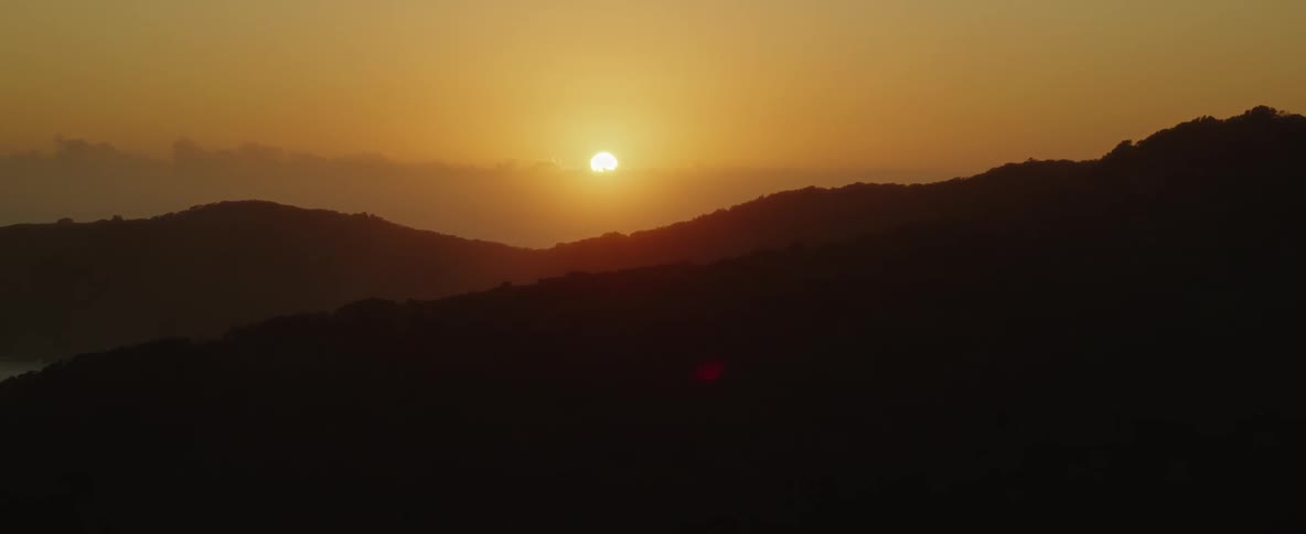 Sun shines from red sky casting mountains into silhouette