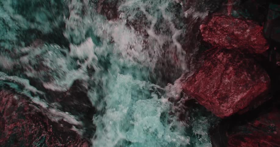 Water foams while flowing past red tinted boulders