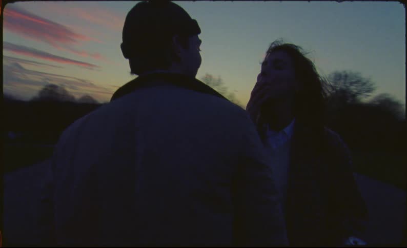 A man and woman kiss outside at twilight