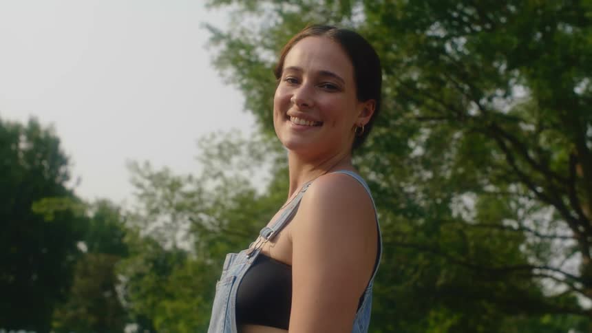Woman standing outdoors near trees turns with a smile