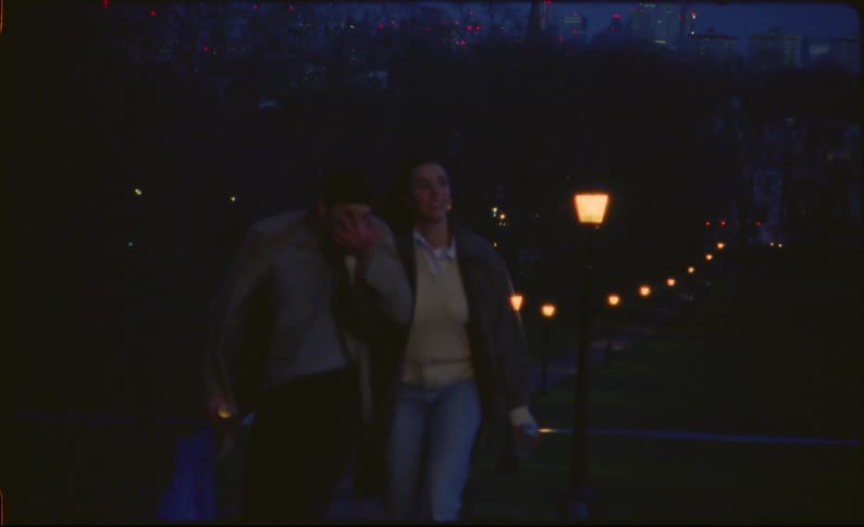 Man kisses woman's hand as they walk hand in hand through park at night