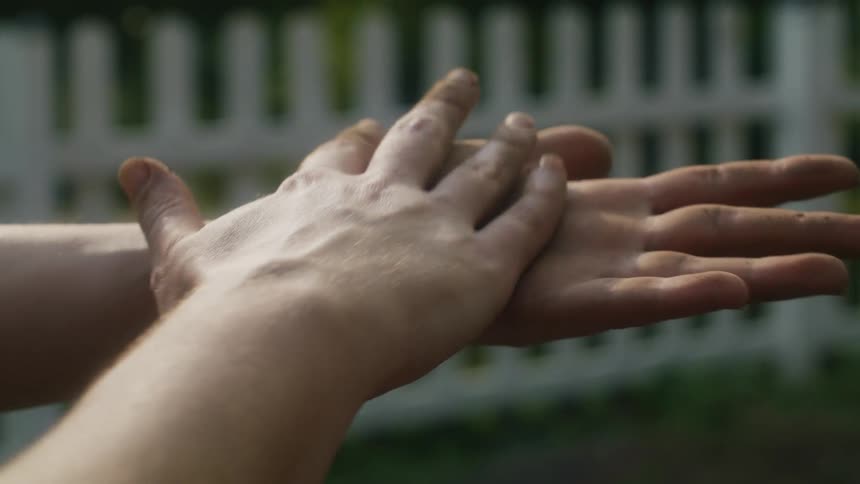 Woman rubs her dirty hands trying to remove dirt while standing in lawn with picket fence