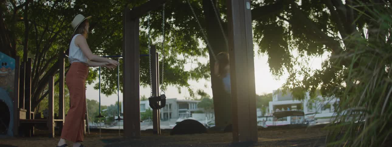 A woman pushes her daughter on a swing at a playground along a lake