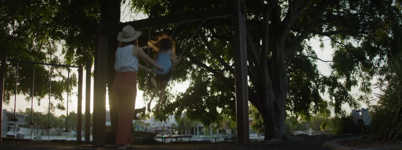 A mother is pushing her daughter on the swing