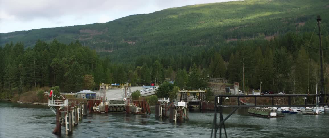 Ferry in a lake leaves a dock near a pine tree forest in the mountains