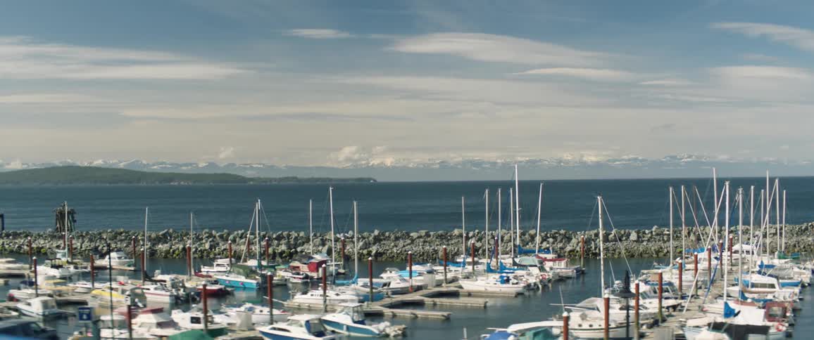 Light fog covers mountains on horizon across water from sailboats moored in marina
