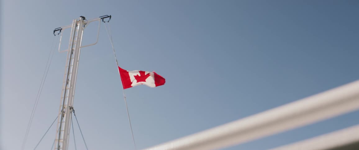 A canadian flag waving in the wind with the sky and clouds in the background