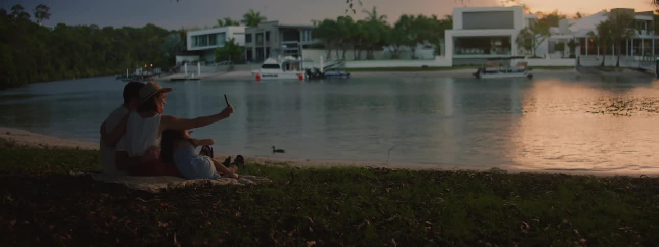 A family of father mother and daughter take a selfie by a lake at dusk