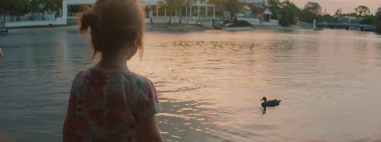 A man films his daughters looking at ducks in a lake