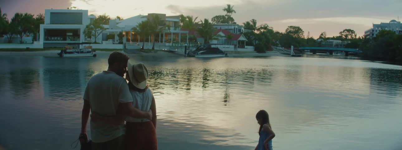 A couple and their young daughter gaze at a lake at dusk then the couple kisses